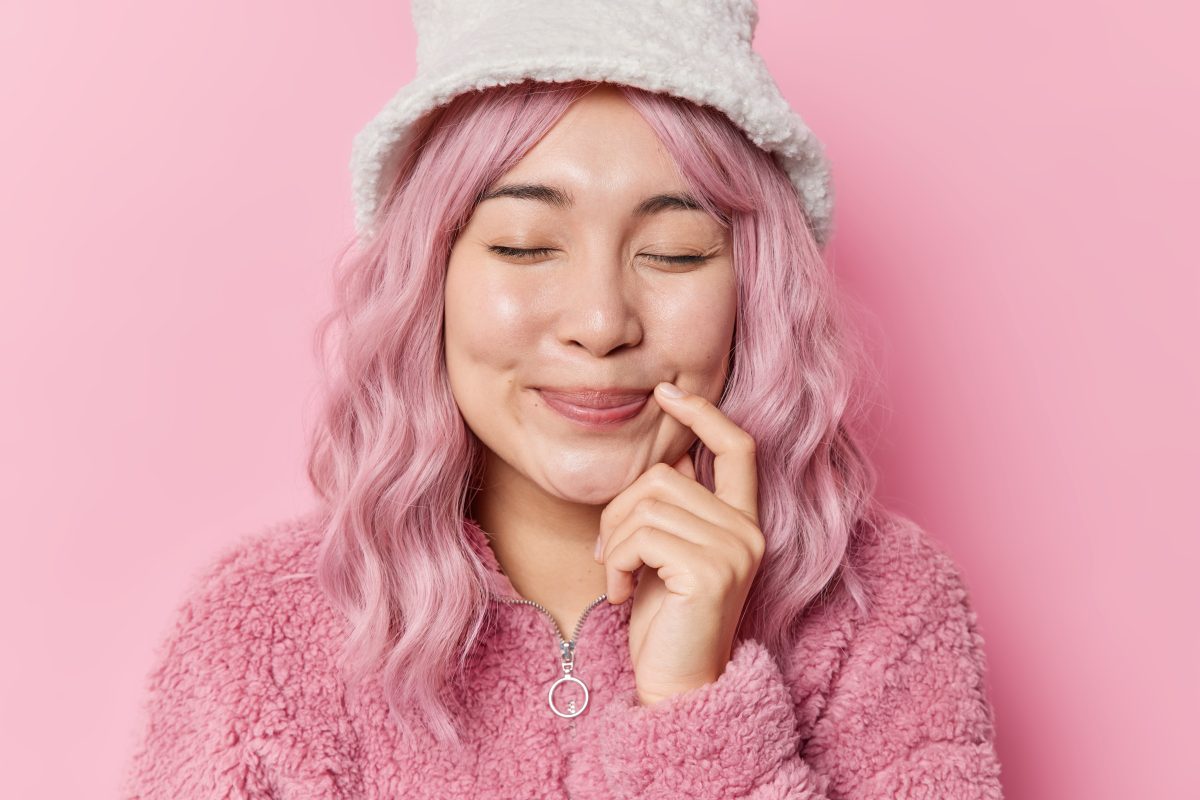 horizontal-shot-dreamy-delighted-asian-woman-closes-eyes-keeps-finger-near-corner-lips-has-pink-dyed-hair-dressed-fur-coat-winter-hat-isolated-pink-background-happy-feelings-1-1200x800.jpg